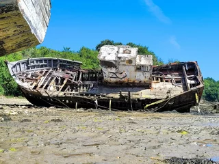 Selbstklebende Fototapeten Rusty ship wreck on muddy rocky beach under blue sky © Wirestock