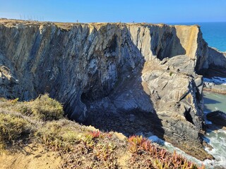 Aerial view of rugged steep cliffs overlooking the sea under blue sky
