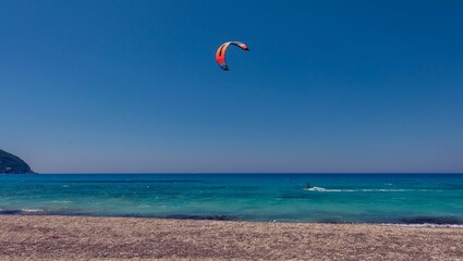 Kiteboarder pulled by a power kite across the sea against a blue sky background