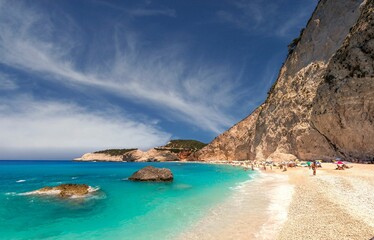Fototapeta premium Beautiful view of a blue sea with people enjoying their vacation on a rocky shore