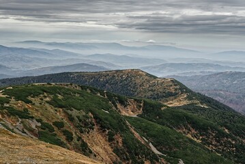 Scenic view of hills with with silhouettes of mountains in background under cloudy sky