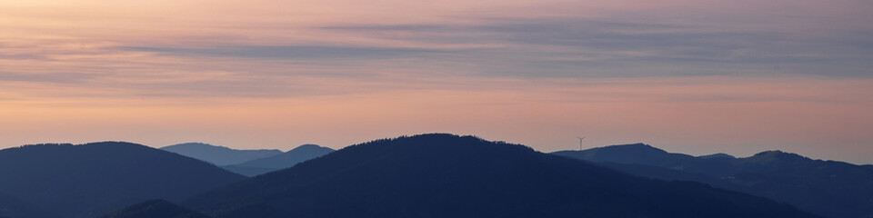 Banner 4x1 Linkedin. Black silhouettes of alpine mountains with windmills on peaks at sunset