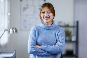  Young Asian business woman smiling confidently while standing alone in a bright modern office