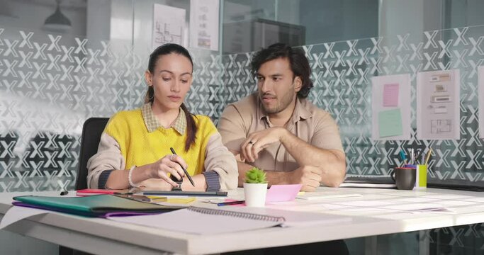 Indian Hindu Asian gen z adult busy woman lady staff sitting chair man trying to kiss make face indoor job office young upset girl use tablet touch pad feel bad male boy boss do flirt abuse affair