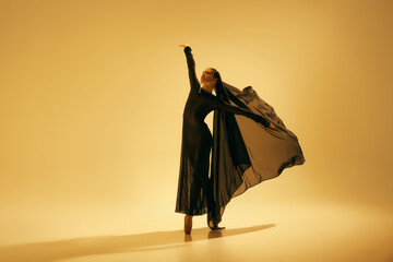 Desert freedom. Elegant and artistic young woman in black attire with veil dancing, performing...