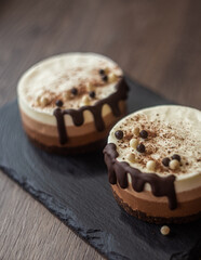 three-layer mousse dessert with chocolate and chocolate chips and crispy balls on a black stone board on a wooden table, close-up with blurred background. food photography, sweets.

