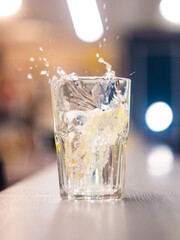 splashes of water from an ice cube falling into a tall rocks glass. glass with ice, lemon and tonic in a thin, high stream. on the bar counter, blurred background
