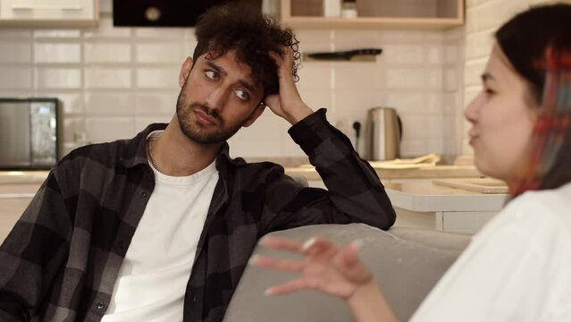 Young woman sitting on a couch at home close up and emotionally tell something to her partner, but he is looking indifferent to her words. Concept of problems in couple relationship