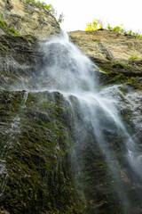 Waterfall hidden inside the forest, beauties of Slovenia to be discovered. Near Nova Gorica, Tolmin village. Water spray and vivid rainbow forms from the waterfall that falls sheer onto the rock.