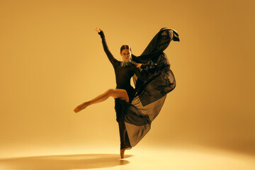Artistic and expressive performance. Young woman, ballet dancer in black flowing attire dancing...