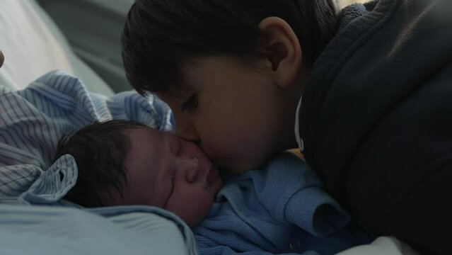 Newborn baby being kissed on the cheek by brother at hospital clinic after birth, first day of infant in the world being welcomed by family in a heartwarming gesture