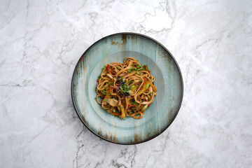 Udon noodles with baked vegetables on a marble table background