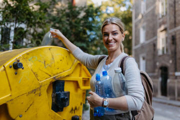 Woman throwing plastic waste, bottles into recycling container in front her apartment. Woman...