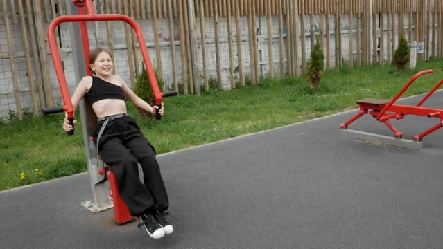 Girl doing arm exercise in outdoor gym. Child training outside on sports ground. Fitness, sport, sportive people concept. Development of strength and endurance of a person. Copyspace