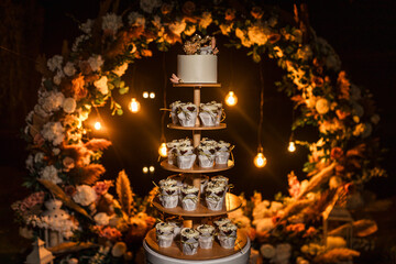 wedding cake on the background of a wedding arch, light bulbs, cupcakes, wedding decor