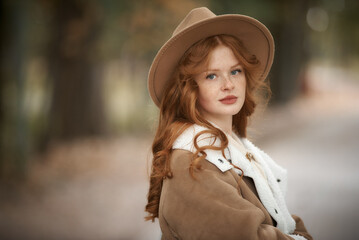 Red-haired girl in a hat and beige coat in the autumn forest. Graine effect used