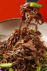 Stir-fried soba noodles with beef and green beans on fork