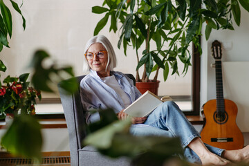 Beautiful mature woman reading book, feeling cozy and happy. Weekend activity for older woman, relaxing at home.