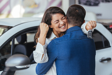 Happy couple embracing after receiving keys from their new car in a showroom. Yay honey, we have bought a new car! Happy couple buying a car at the dealership and holding the keys