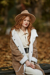 Red-haired girl in a hat and beige coat in the autumn forest. Graine effect used