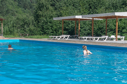 A heated pool high in the mountains. Relaxing by the water in the fresh air. Sun loungers for relaxing and sunbathing near the blue water pool. A girl and a young man are swimming in an open-air pool.