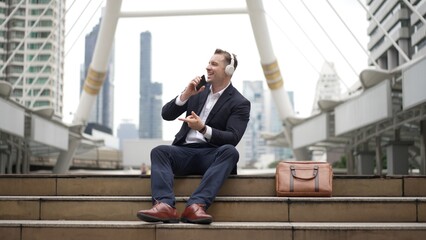 Professional business man listening headphone and using phone record voice while sitting at stair...