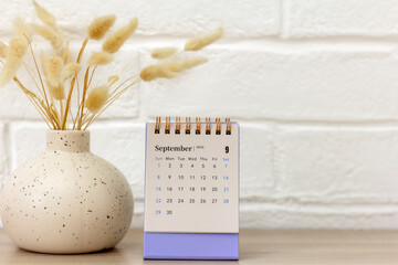 Calendar for September 2024 and a vase with dried flowers on the table.