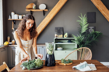 A charming curly-haired brunette girl in a linen sundress prepares a healthy green smoothie in a...