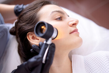 Doctor dermatologist examines skin of client face of beauty salon with a dermatological lens