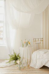 beautiful bedroom interior with a bed and curtains in white colors and with green plants in pots....