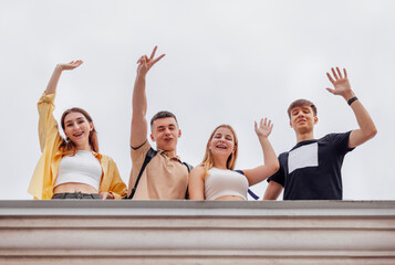 Four teenagers in casual clothes waving and laugh on the roof of the house