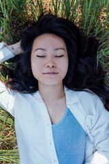 Asian woman in a white shirt and a gray top lies on the grass and laughs