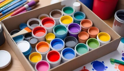 A box containing an assortment of colorful paints and various paint brushes scattered around