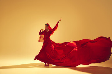 Elegance and passion. Female artistic dancer wearing red flowing dress and making performance...