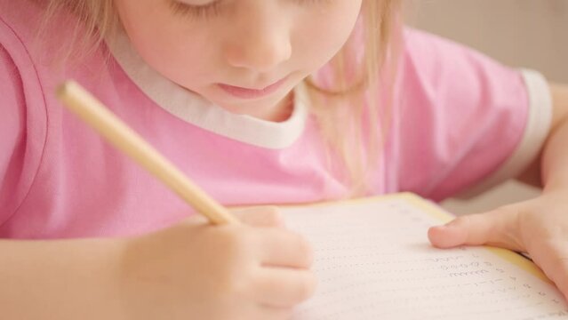 small child, blonde girl 5 years old learning to write in workbook, child's hand holding pencil, preschooler practices writing letters in notebook, Early childhood development