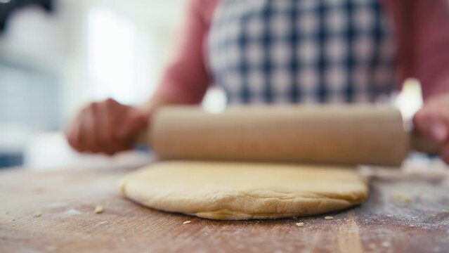 Close up of woman in kitchen rolling out dough with rolling pin on wooden board to make pasta - shot in slow motion