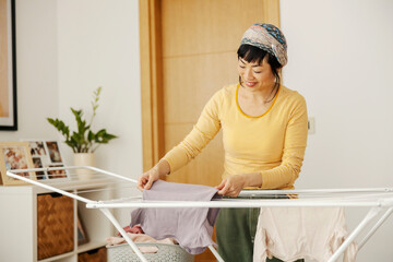 A happy neat japanese middle aged woman putting laundry on a rack at home.