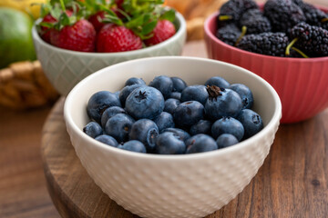Blueberries, black mulberries and strawberries in fruit cups next to the fruit basket on a wooden surface