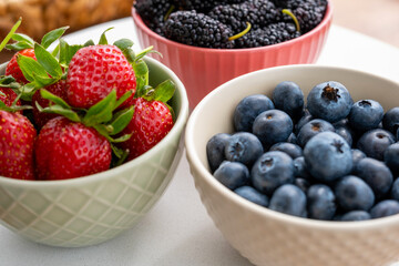 Blueberries, black mulberries and strawberries in fruit cups next to the fruit basket on a marble...
