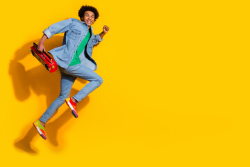 Full size portrait of nice young man boombox run jump empty space wear denim shirt isolated on yellow color background