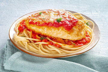 Chicken Parmesan, Italian pasta dish. Breaded chicken breast with cheese and spaghetti with tomato sauce, with parsley, on a table