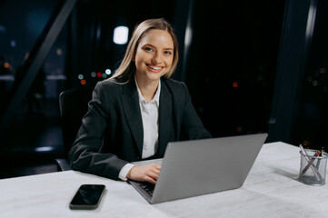 Portrait of a young businesswoman sitting at her desk using a laptop, working in the office late at night