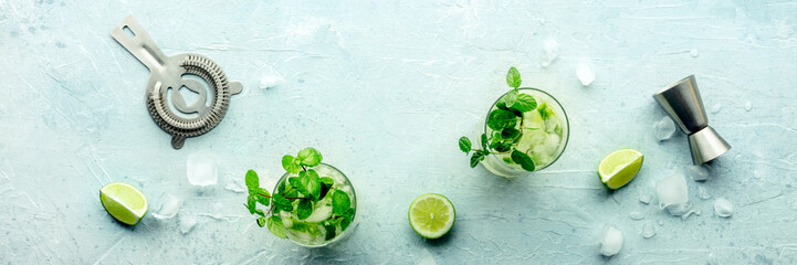 Mojito cocktail, overhead flat lay panorama. Summer cold drink with lime, fresh mint, and ice. Cool beverage with mixing accessories