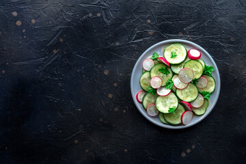 Fresh cucumber and radish salad with parsley, overhead flat lay shot. Simple vegan recipe on a slate background. Healthy diet, with copy space