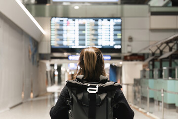 Young woman backpack in international airport terminal looking at the flight schedule information...