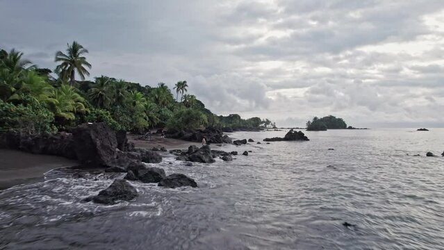 An idyllic beach with blonde woman on black sand and palm trees