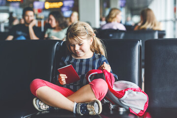 Little girl at the airport waiting for boarding at the big window. Cute kid holding...