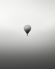 Obraz premium hot air balloon ascending through a misty morning sky. The simplicity of the composition and ethereal atmosphere, minimalist black and white photograph