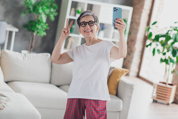 Photo of lovely mature lady selfie photo v-sign dressed white garment modern living room rest enjoy...
