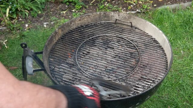 Gloved hand Cleaning burnt food on dirty barbecue grill grates with brush